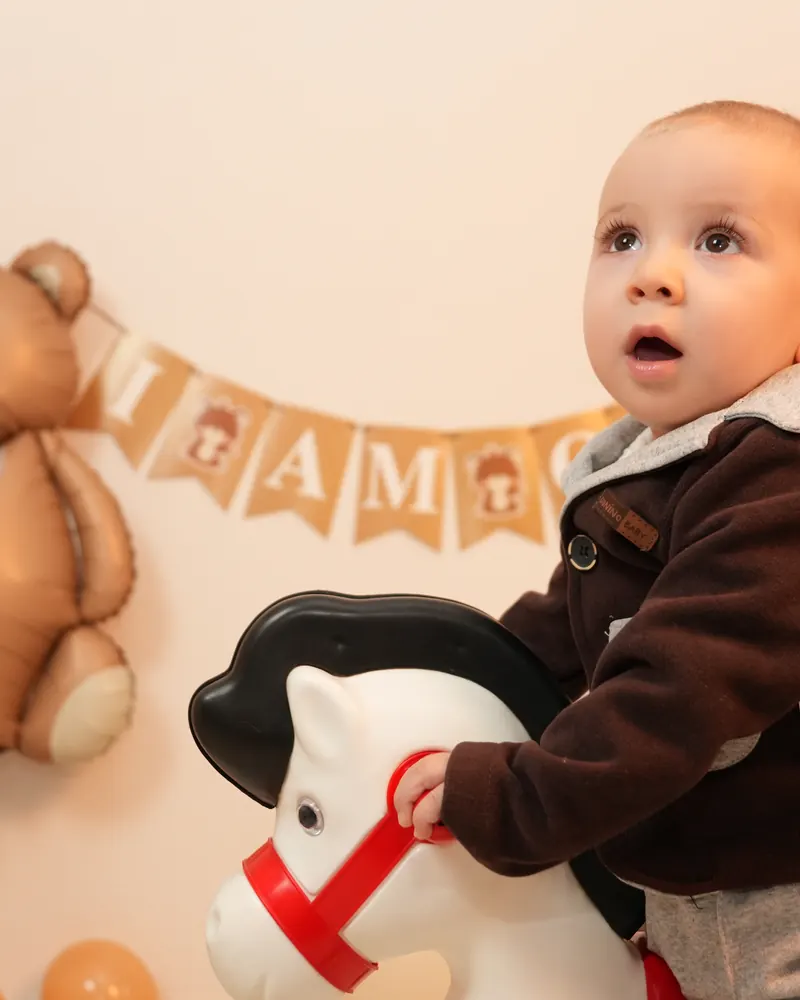 Ayıcık balonu ve süslemelerin önünde oyuncak sallanan atına binen bebek