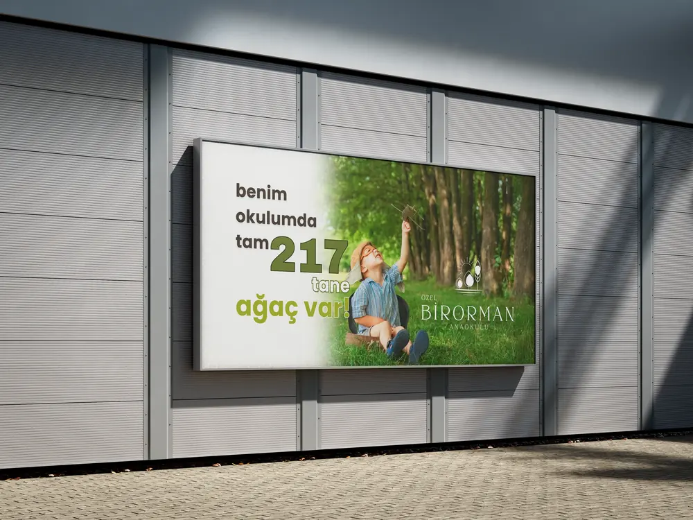 Bir anaokulu için doğa temalı billboard: ağaçlar arasında oynayan çocuk ve “benim okulumda tam 217 tane ağaç var” mesajı