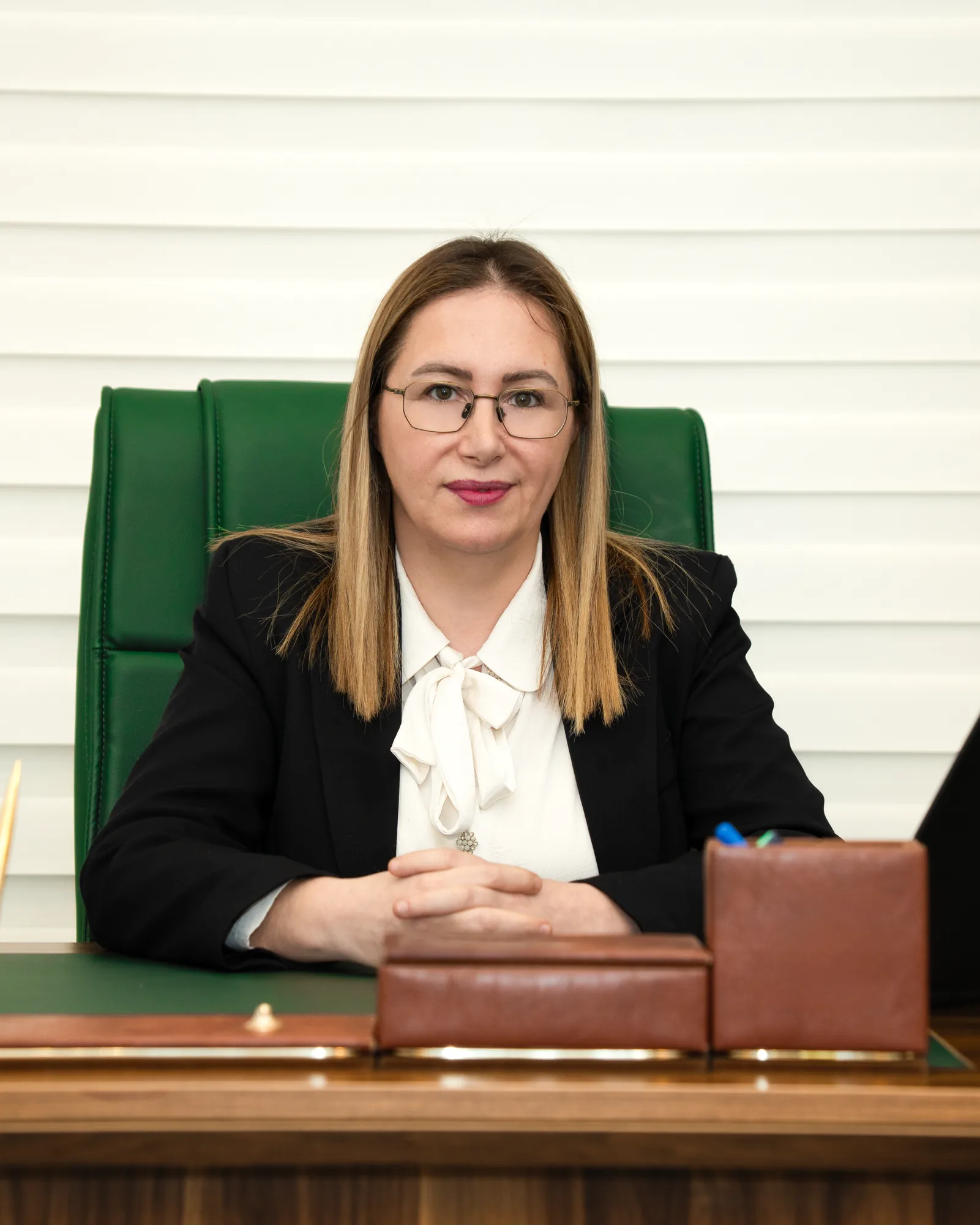 Mahiroğlu Hukuk & Danışmanlık avukatı yeşil deri koltukta, masasında oturur portre